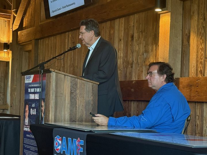 Stephen Petty presenting from the podium with Scott Smith seated
